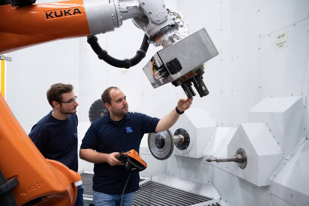 Bild 1 | Christian Kunz (r.) und Christian Haase (l.) inspizieren die Greifer eines Roboters. Diese sollen später schwere Motorgussteile an die Bearbeitungsstationen halten, die rechts aus der Wand ragen.
