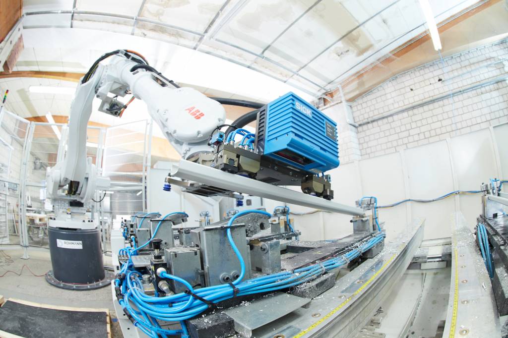 Zwei Industrieroboter bestücken eine automatische Bohr- und Fräsmaschine mit Aluminiumprofilen verschiedener Länge.