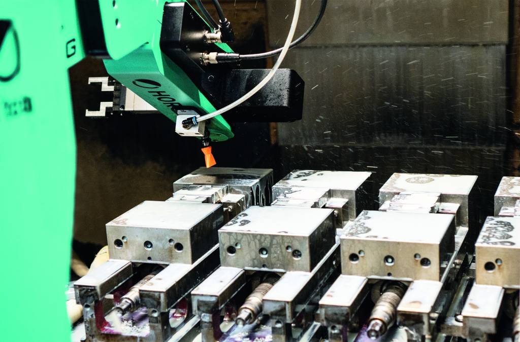 Wenn die Bearbeitungsmaschine das Fertig-Signal an den Sechsacher Horst900 von Fruitcore Robotics sendet, betätigt er einen Zylinder, öffnet die Maschinentür, fährt in die Maschine ein und reinigt das Werkstück.