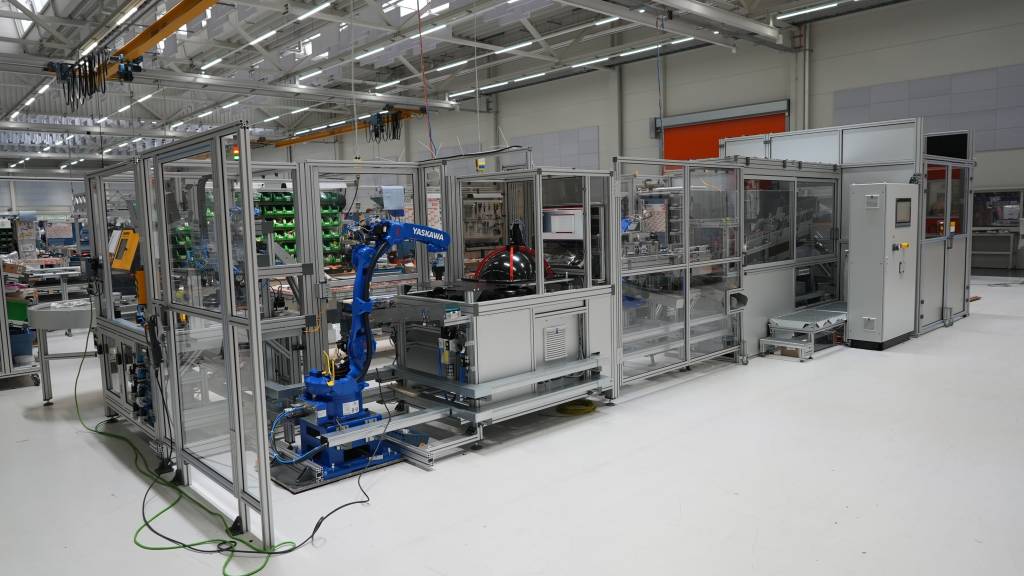 In einer Anlage für ein Unternehmen aus der Umformtechnik übernimmt ein Roboter mit Doppelgreifer ein Bauteil und übergibt es an eine Messeinrichtung.